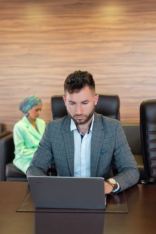 Free Businessman focused on work, sitting at a desk with a laptop in a modern office setting. Stock Photo