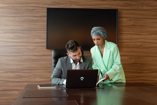 Free Two business professionals collaborate at a desk with a laptop in a modern office setting. Stock Photo