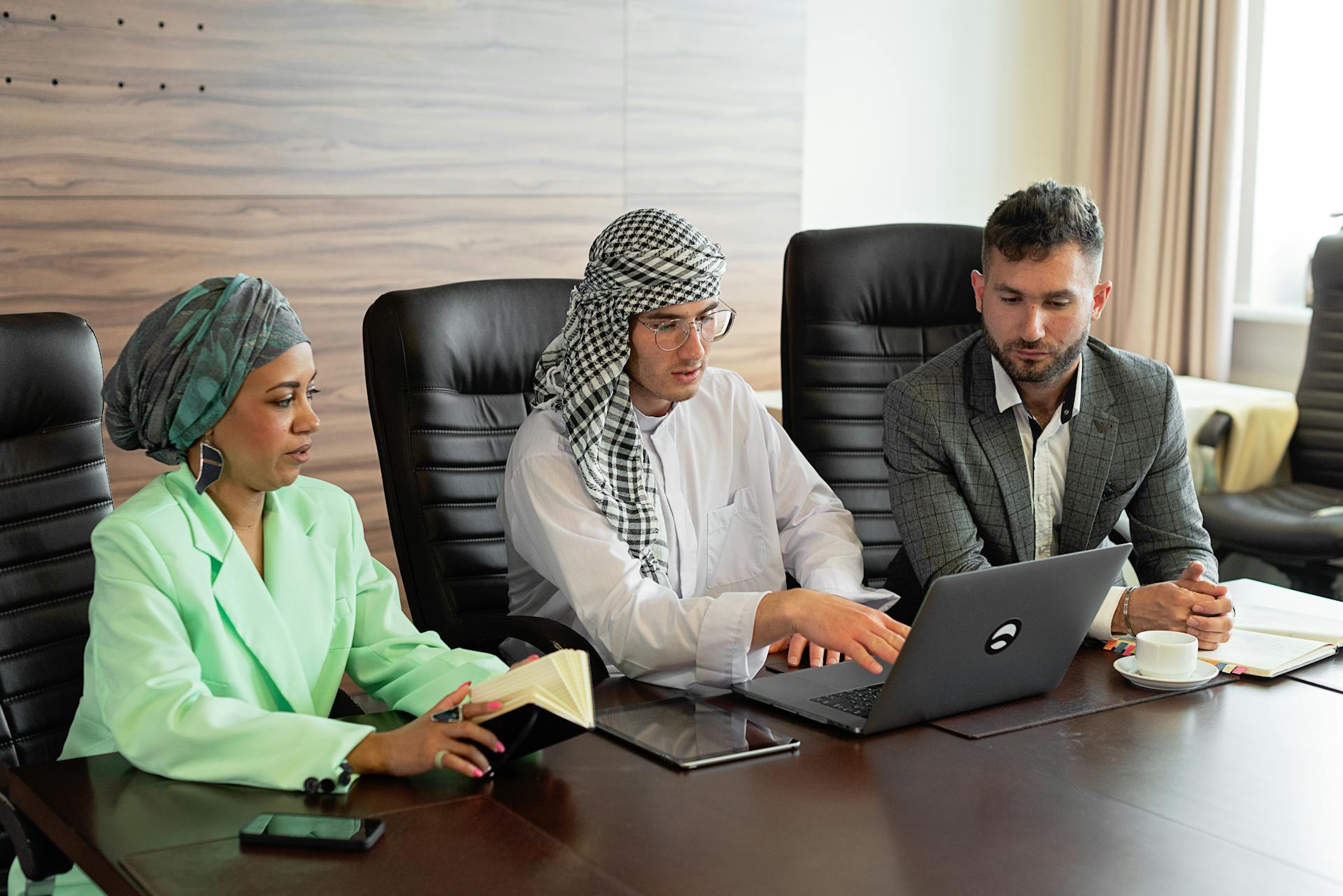 Three business professionals discussing over a laptop in a modern office setting.