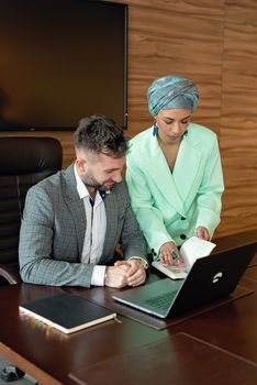 Professional teamwork with a man and a woman in hijab discussing projects at a laptop.