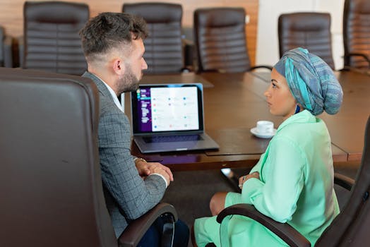 A man and woman discussing business plans in a conference room with a laptop.