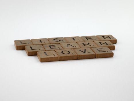 Wooden letter tiles spelling 'listen, learn, love' on a white background, encapsulating key life values.
