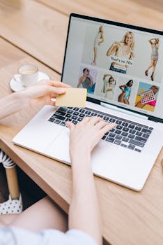 Hands holding a credit card while online shopping on a laptop at a wooden table.