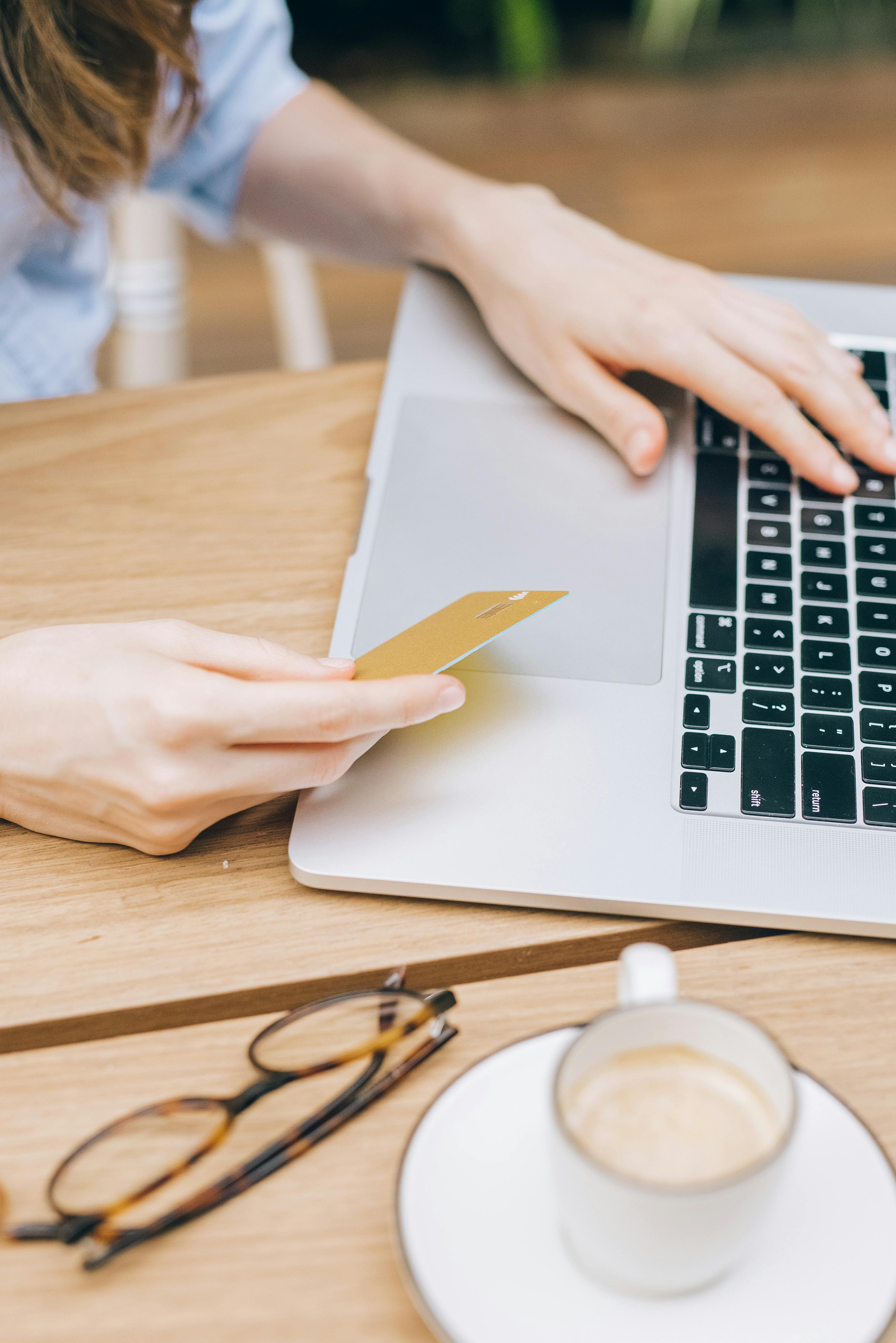 a person typing on laptop while holding a credit card