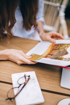 Woman reading a magazine, with eyeglasses and notebook on wooden table.