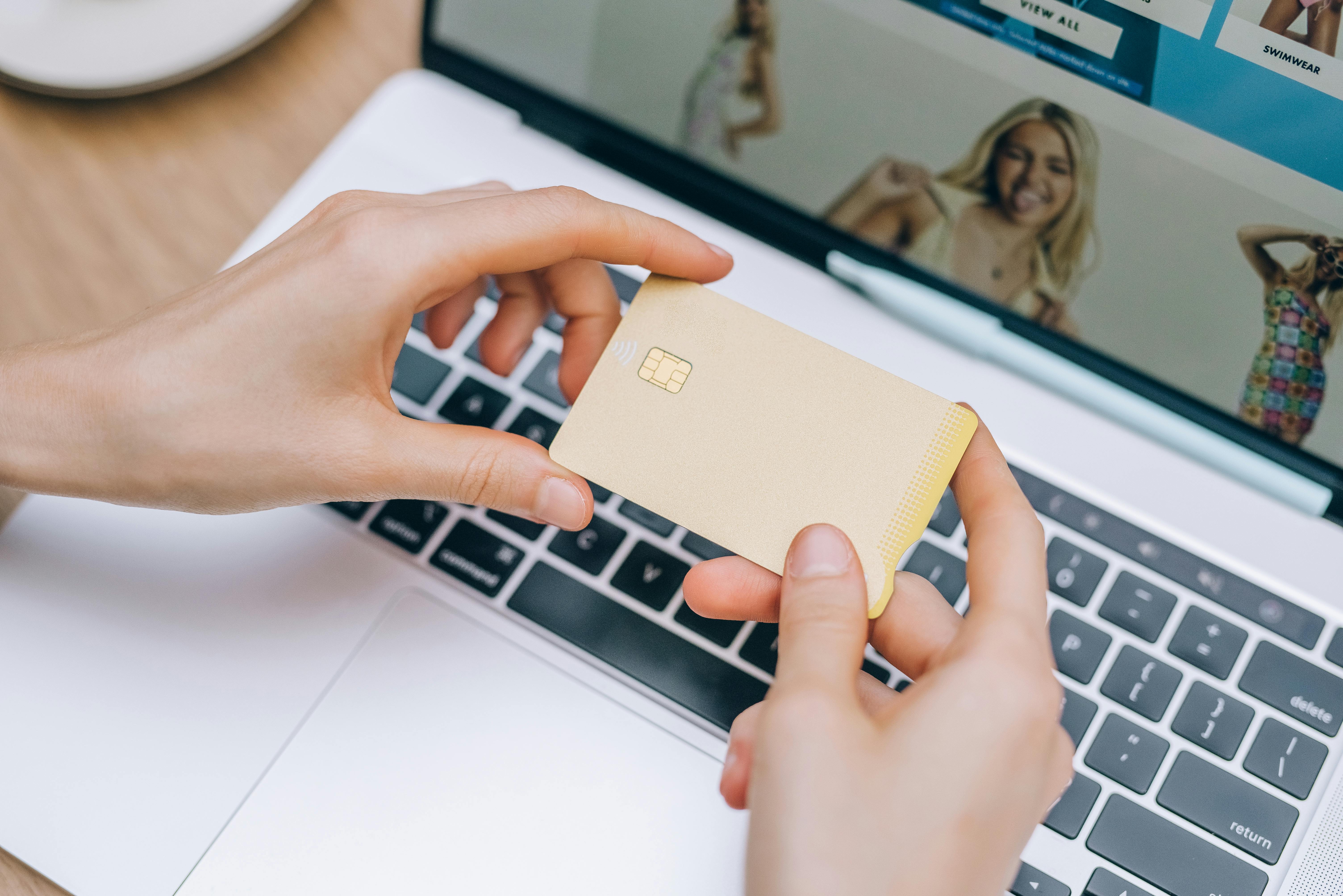 person holding a credit card near a laptop