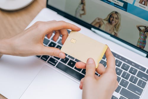 Person Holding a Credit Card Near a Laptop