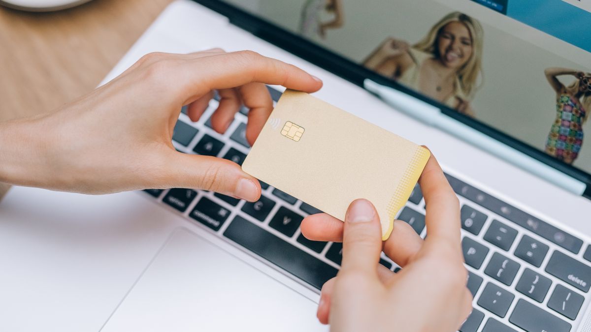Hands holding a payment card beside a laptop