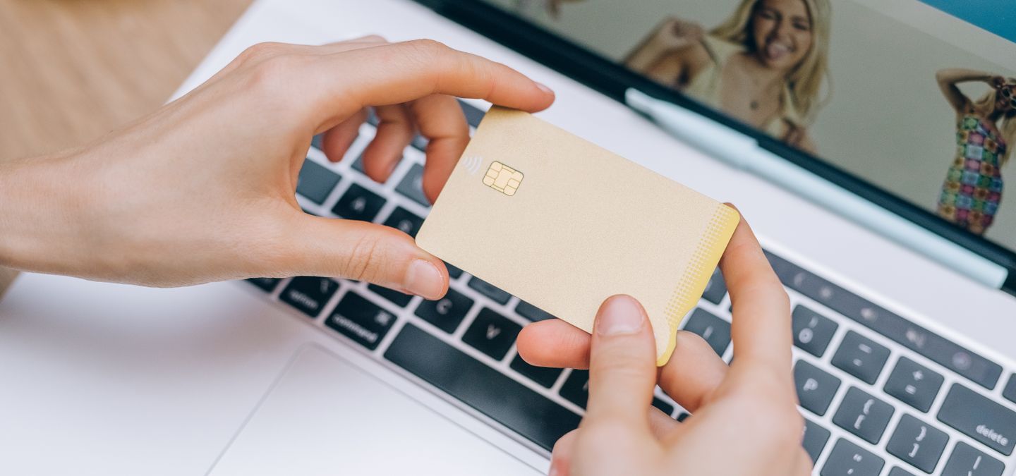 Hands holding a payment card beside a laptop