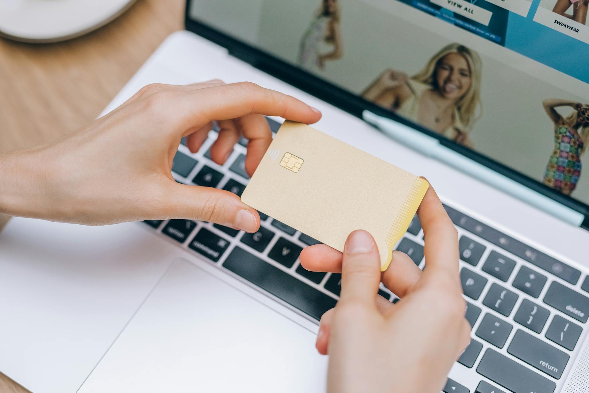 Person Holding a Credit Card Near a Laptop