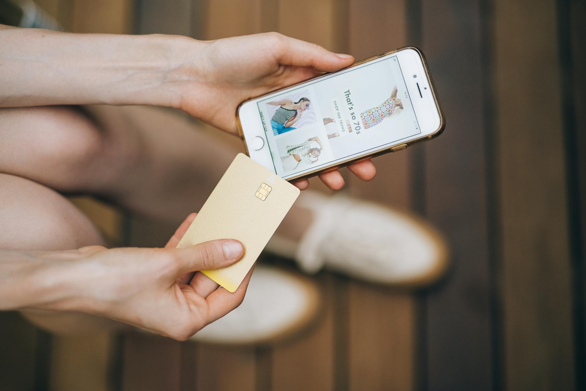 Hands holding smartphone and credit card for online shopping on a wooden floor.