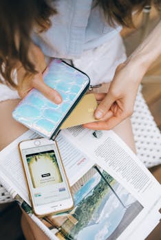 Adult woman using credit card and smartphone while reading a book outdoors.