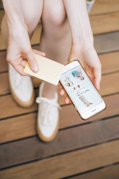 Close-up of a person holding a credit card and smartphone for online shopping, featuring a trendy app interface.