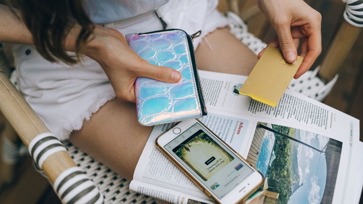 A woman uses her smartphone and credit card for online shopping while sitting outdoors.