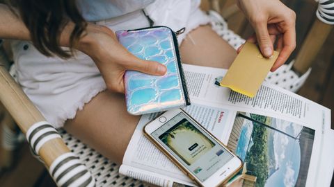 A woman uses her smartphone and credit card for online shopping while sitting outdoors.
