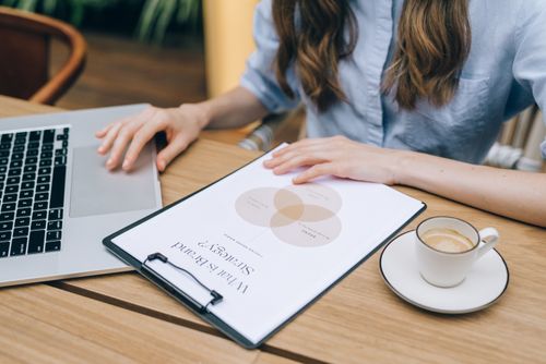 Free A person reviews a brand strategy document on a clipboard while using a laptop in an office setting. Stock Photo