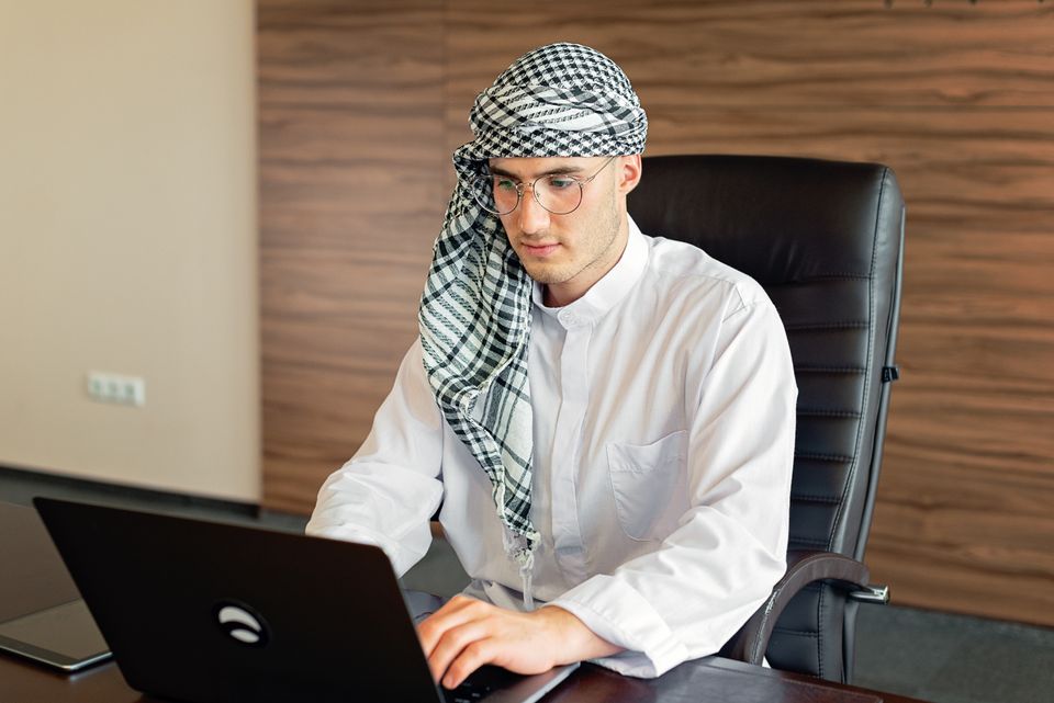 Emirati professional in a kandura working on a laptop