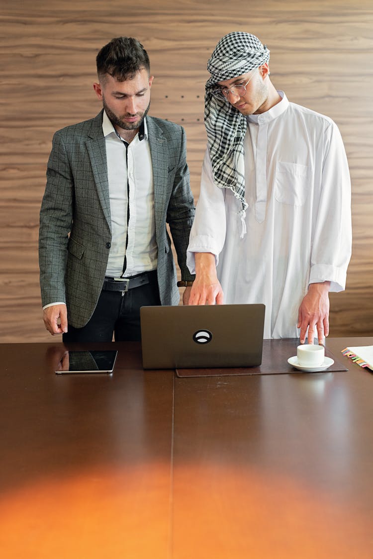 A Man In Gray Suit Jacket Standing Beside A Man Wearing Thawb And Turban