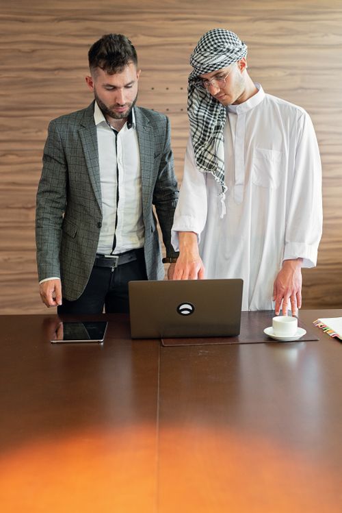 Free Two businessmen in traditional and modern attire working together on a laptop indoors. Stock Photo
