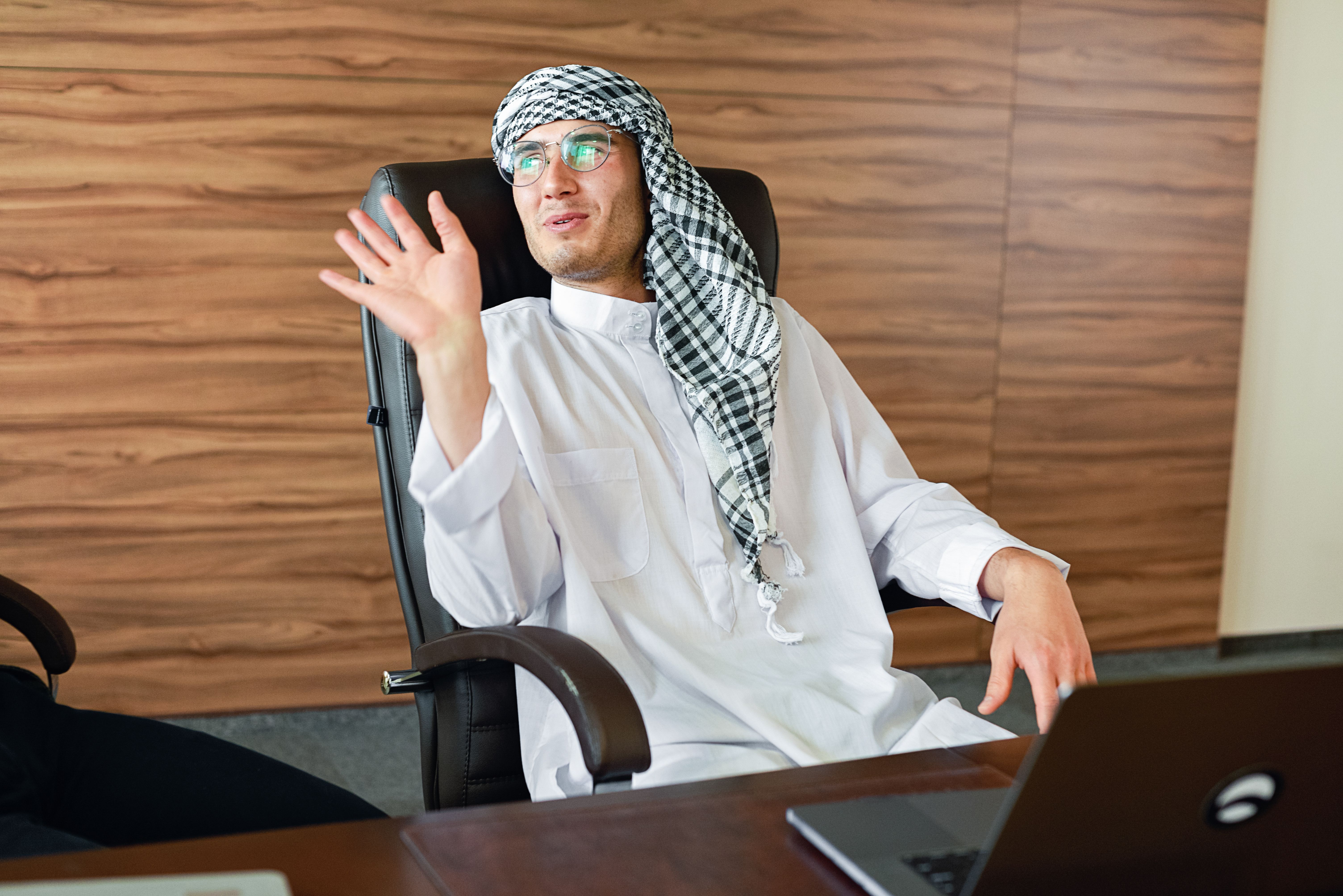 Middle Eastern man in a headscarf gesturing in a modern office setting.