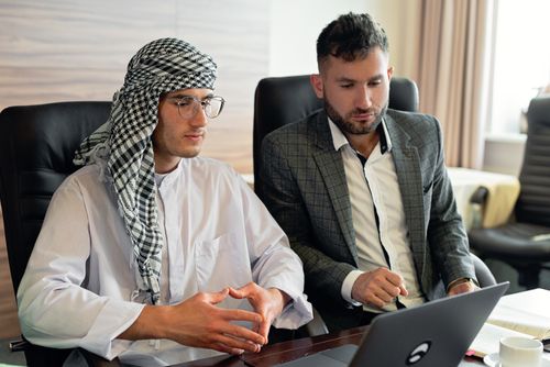 Free Two businessmen in suits collaborate on a laptop in a modern office setting, focused and engaged. Stock Photo