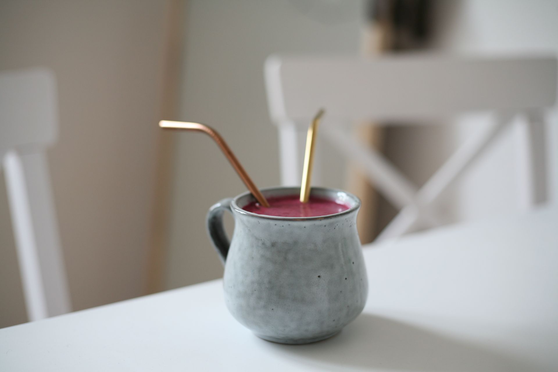 Close-up of a fruit smoothie in a ceramic mug with metal straws on a white table.