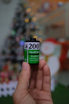 Close-up of a hand holding a Fujifilm 35mm camera roll with holiday decor in the background.