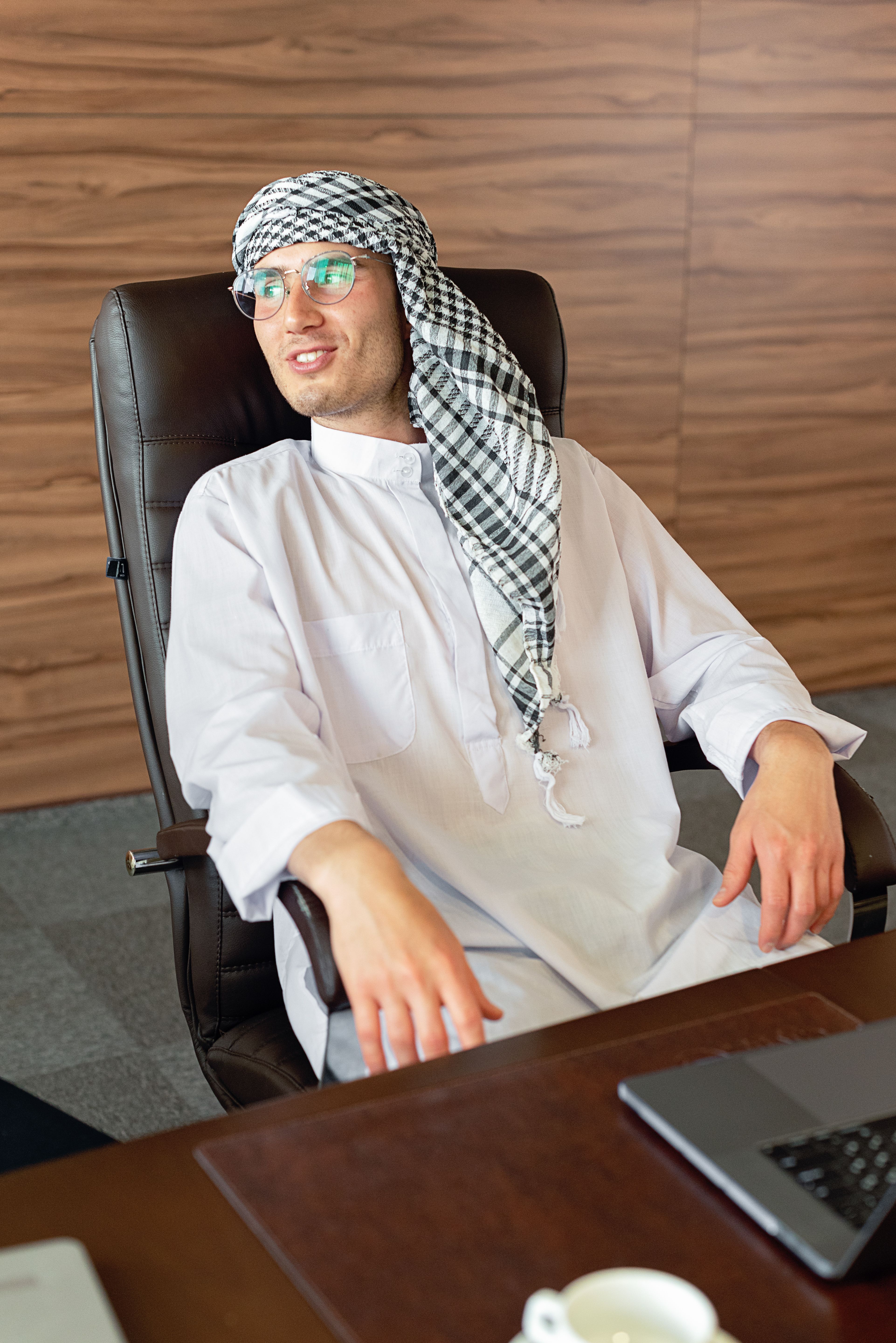 Middle Eastern man in traditional attire sitting relaxed in a modern office chair.