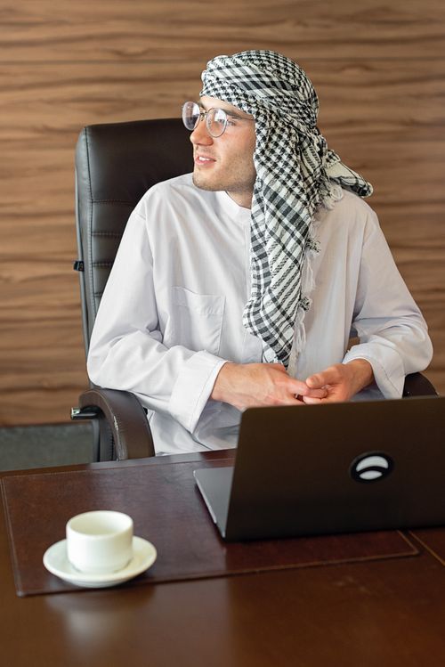 Free A Middle Eastern businessman in traditional attire working at a desk with a laptop in an office. Stock Photo