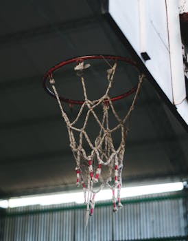 Detailed view of a basketball hoop with worn net indoors, capturing the essence of sports.
