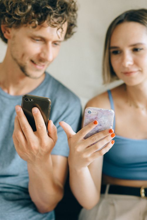 Free A close-up of a young couple sitting indoors, using smartphones together. Stock Photo