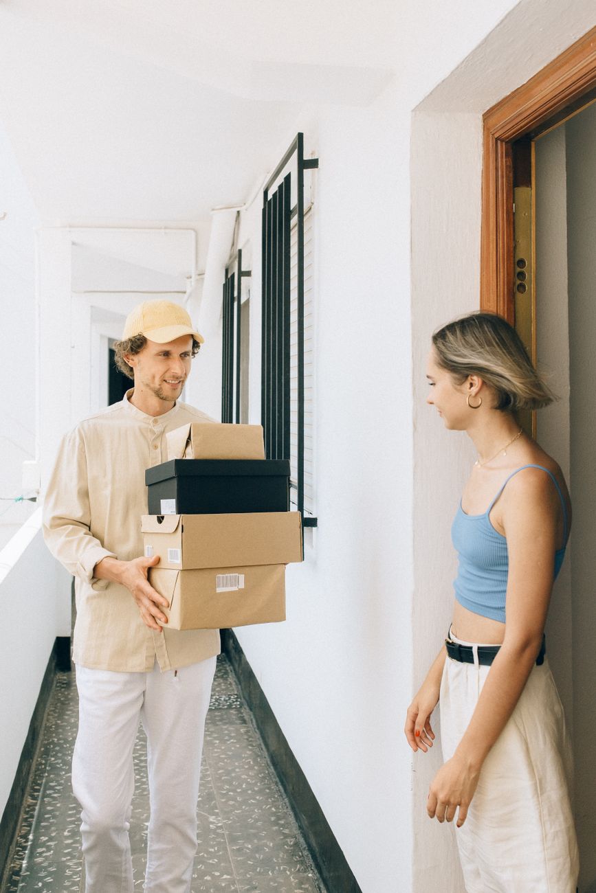 Delivery man handing several packages to a young woman at her apartment door.