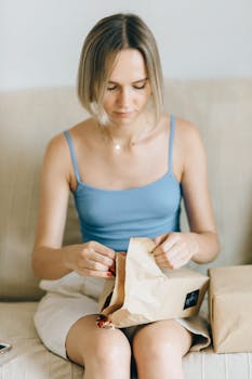 Young woman sitting on couch eagerly opening a delivery package. Online shopping experience.