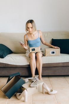 Woman sitting on a sofa with shoes and boxes, shopping online with her phone.