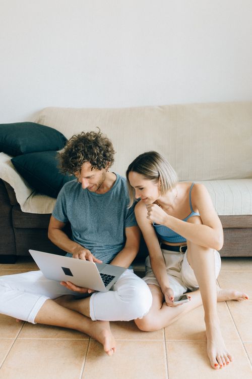 Free A couple sits barefoot on the floor at home, sharing a laptop for online shopping. Stock Photo