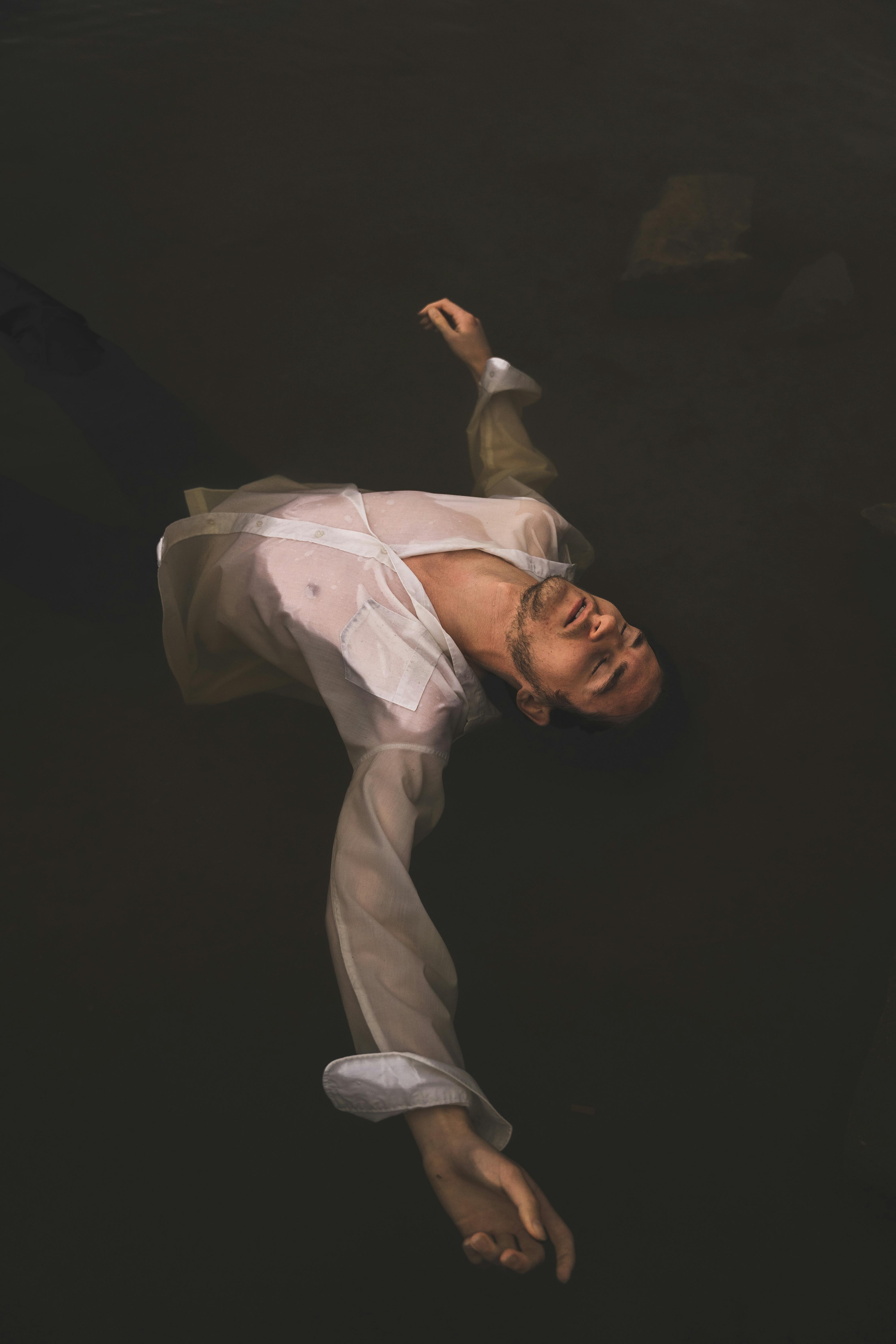 A man in a white shirt floats serenely in dark water, creating a tranquil mood.