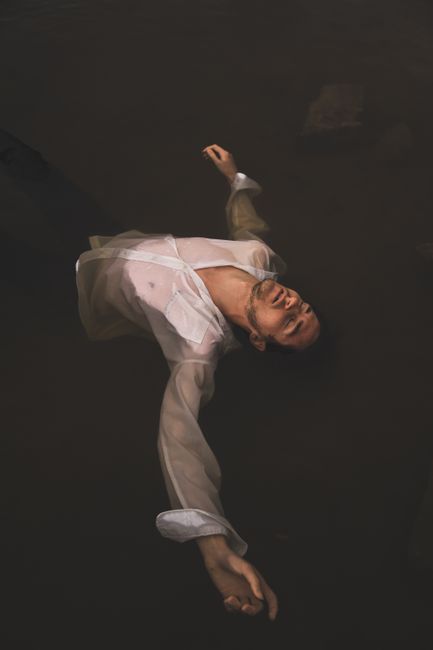 A man in a white shirt floats serenely in dark water, creating a tranquil mood.