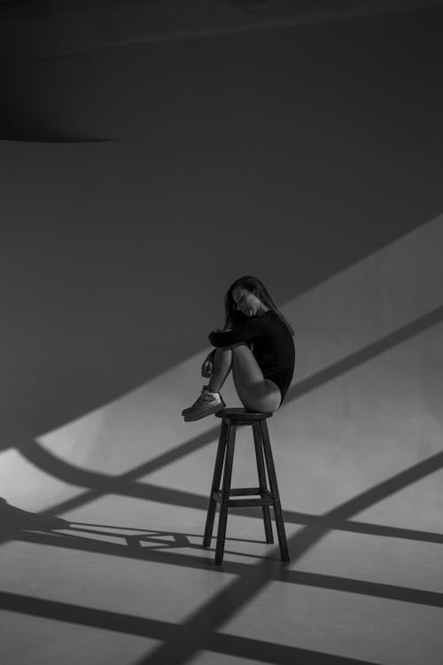 Grayscale Photo of a Woman Sitting on a Stool