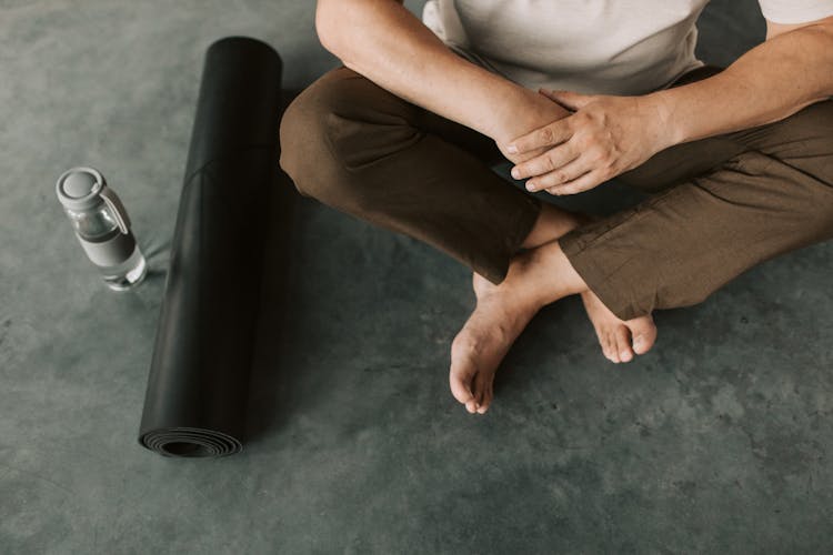 A Person Sitting Beside A Black Yoga Mat