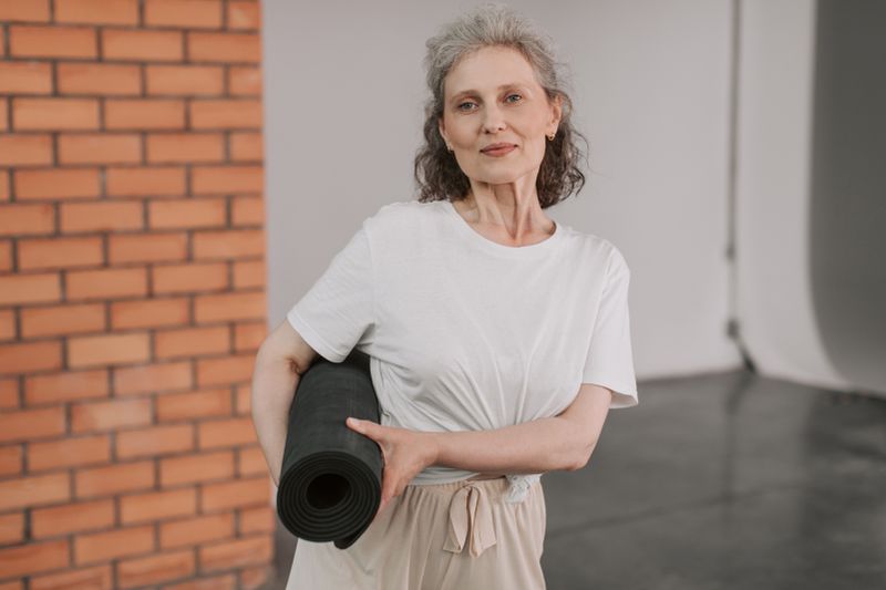 A cheerful senior woman holding a yoga mat, embracing a healthy lifestyle indoors.
