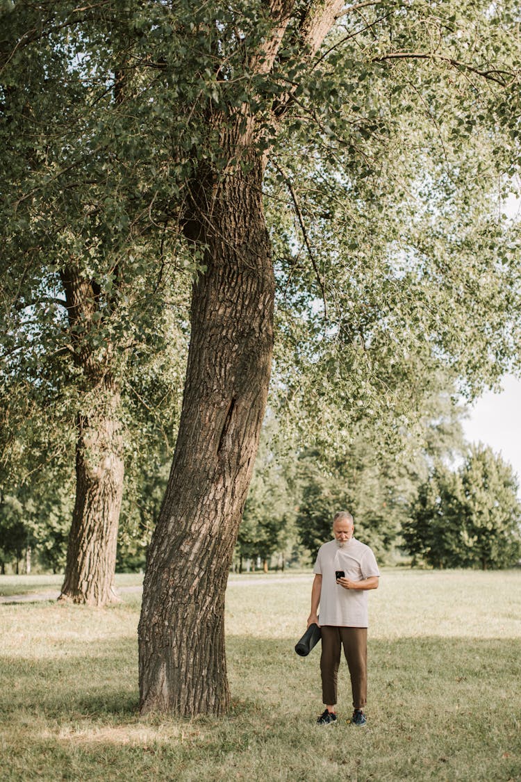 A Man Standing Beside A Big Thick Tree