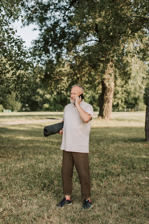 Free Elderly Man Talking on the Phone While Holding Yoga Mat Stock Photo