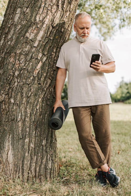 Free An Elderly Man Leaning on a Tree Trunk While Texting  Stock Photo