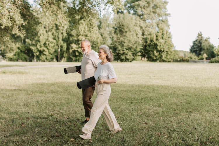 An Elderly Man And Woman Carrying Yoga Mats While Walking 