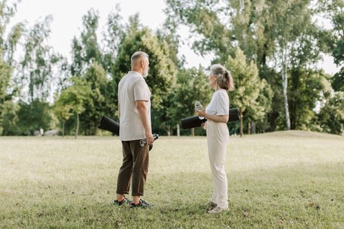 Free Two senior adults holding yoga mats and interacting in a sunny park setting. Stock Photo