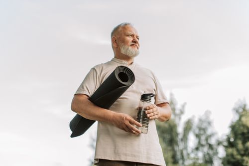 Free Elderly man with white hair holding a yoga mat and water bottle outdoors. Stock Photo