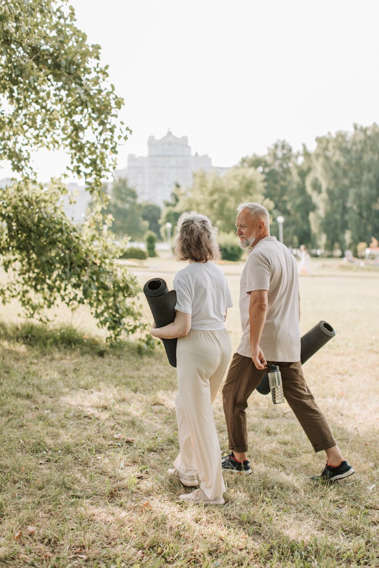 An Elderly Couple Walking Together While Carrying Rolled Yoga Mats And A Water Bottle