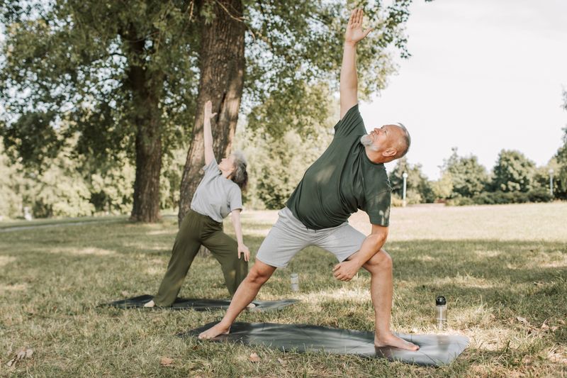 Personas entrenando al aire libre sobre colchonetas en un parque, en postura de estiramiento guiado.