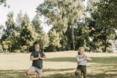 Elderly couple practicing yoga poses on mats in a sunny park setting.