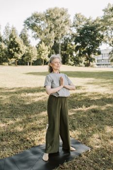 Senior woman practicing yoga in a serene park setting, embracing a healthy lifestyle.
